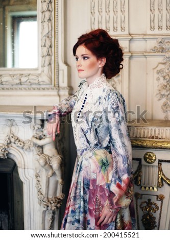 woman dressed in a dress in the palace posing next to the fireplace