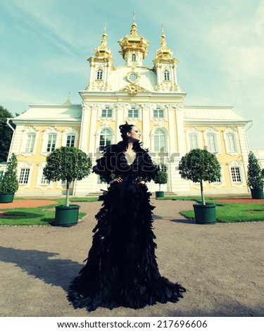 Beautiful woman in black dress posing next to the palace. Dark Queen.
