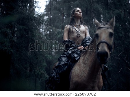 Young man with long hair with horse in dark forest.