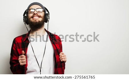 life style, education and people concept:  young bearded man listening to music while standing against grey background. Hipster style.
