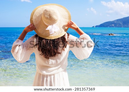 Young woman in summer dress with  straw hat looking to a sky and sea