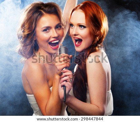 Karaoke party. Beauty girls with a microphone singing and dancing over dark background.