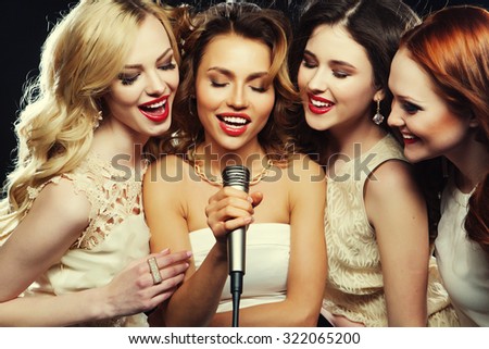 Four beautiful stylish girls singing karaoke at the club