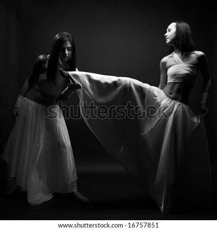 Portrait of two girls in white raiment dancing in semi-darkness. Foot worship.