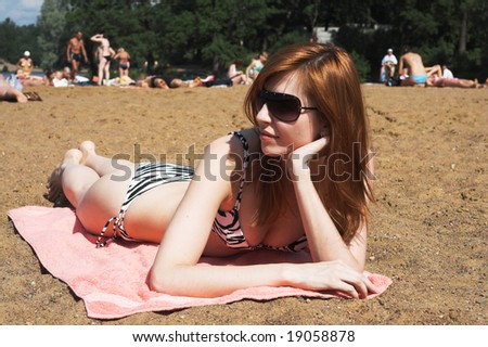 Young beautiful woman in sunglasses and bikini laying on sea beach