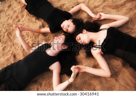 Two girls and a boy laying on the sand hand in hand