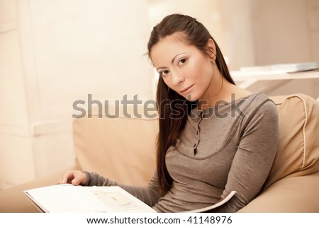 A young woman reads a magazine while sitting on her couch