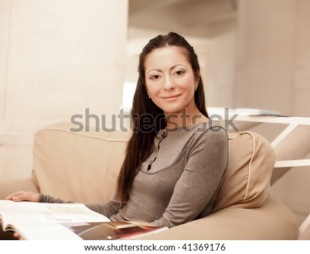 A young woman reads a magazine while sitting on her couch