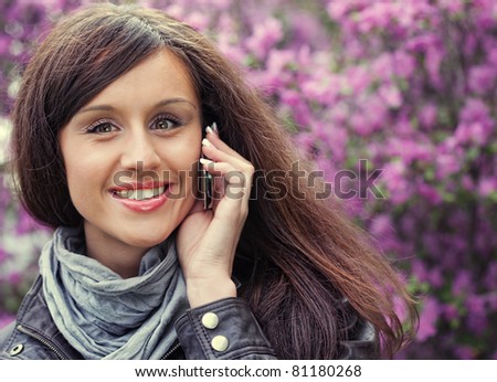 Beautiful smiling girl speaks by mobile phone against summer flower nature.