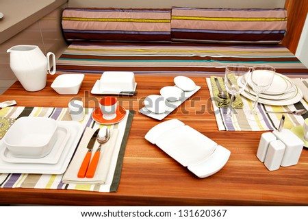 Modern kitchen table laid with dishes, utensils and striped mats.