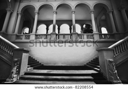 Black and white image of a classical architectural structure. Two symmetrical stairs and five arches in the front and five in the back.