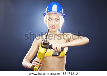 Beautiful topless model holds a power drill while wearing a blue construction helmet.
