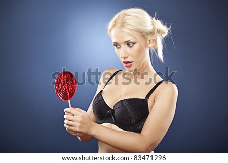 Beautiful blonde model, in black bra, looks at a red lollipop.