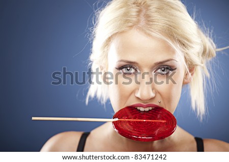 Beautiful blonde model, in black bra, bites into  a red lollipop.
