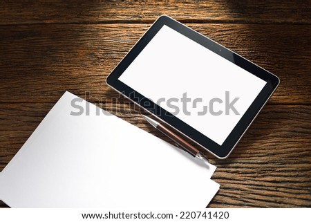 Tablet computer and white papers on old wooden table