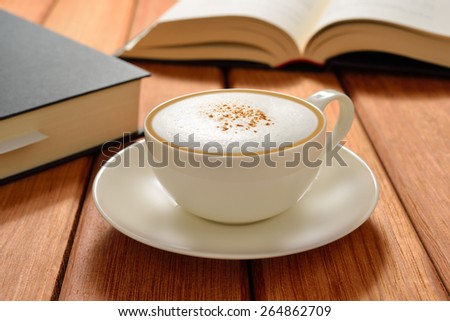 Cup of cappuccino coffee and books on wooden table