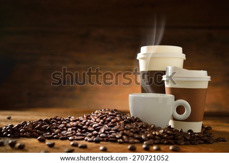 Cups of coffee with smoke and coffee beans on old wooden background