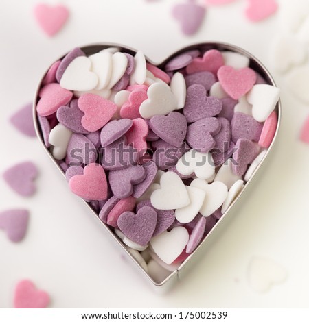 Heart shaped candy sweets used for cake decoration in a tin with several loose sweets faded out in the background