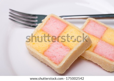 Battenburg cake, pink and yellow sponge squares wrapped in a marzipan coating, sliced on a plate with a fork