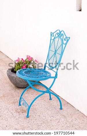 Blue cast iron cafe style chair next to a plant pot with flowers in it.