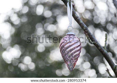 Christmas glass decoration hanging outside on the branch of a tree. Back lighting has caused a bokeh effect behind the bauble.