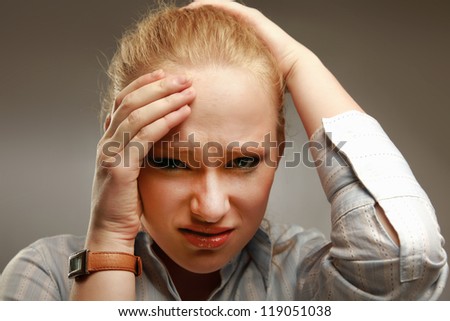 A young woman with a headache holding head, isolated on grey background