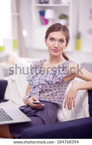 Young smiling beautiful woman sitting on the sofa with phone and laptop