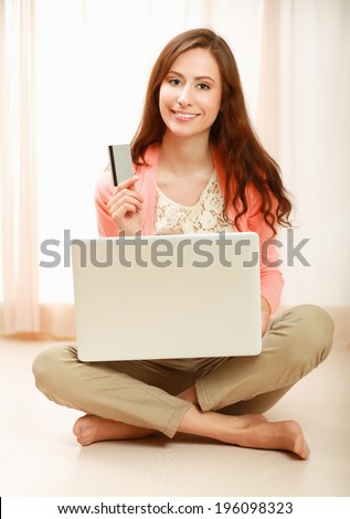 Young woman sitting on thr floor with laptop and holding credit card