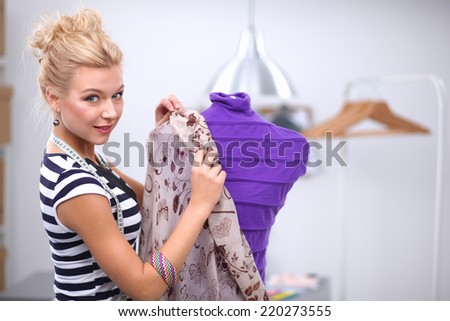 Smiling fashion designer fixing dress on  mannequin in a studio