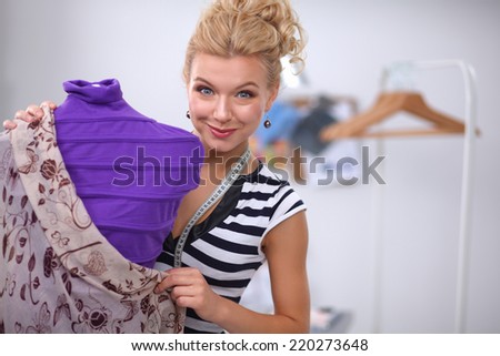 Smiling fashion designer fixing dress on  mannequin in a studio