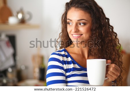 Portrait of young woman with cup against kitchen interior background.