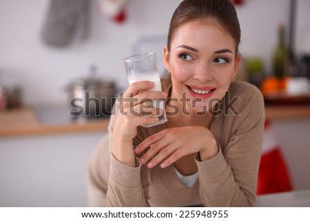 Smiling young woman drinking milk, standing in the kitchen