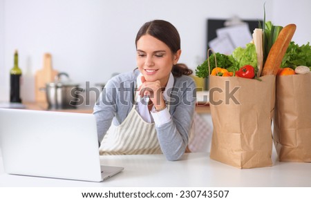 Beautiful young woman cooking looking at laptop screen with receipt in the kitchen