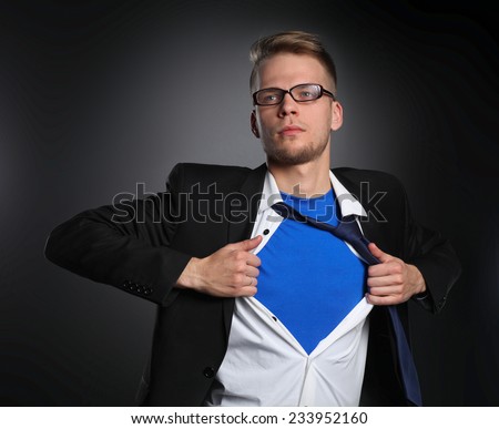 Young businessman acting like a super hero and tearing his shirt, isolated on gray background