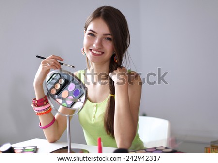Young beautiful woman making make-up near mirror,sitting at the desk
