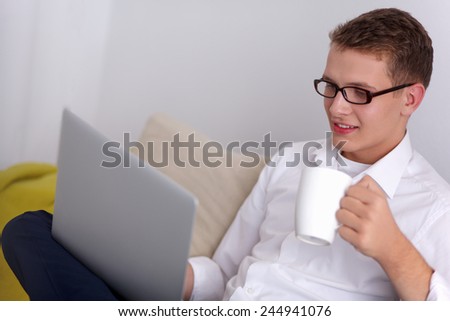 Relaxed attractive man holding coffee while working on his laptop in bright living room