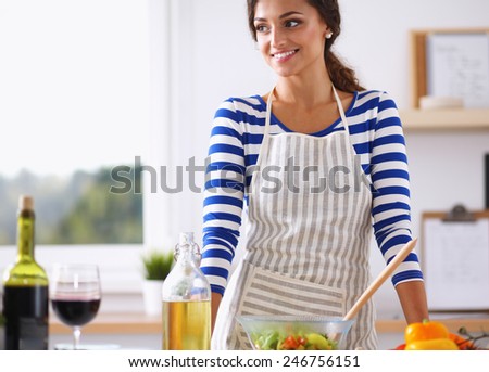 Smiling young woman  mixing fresh salad, standing near desk