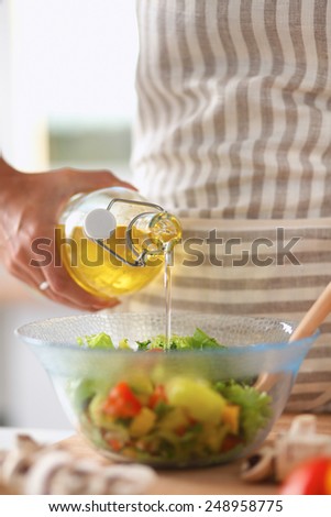 Smiling young woman  mixing fresh salad, holding bottle of oil