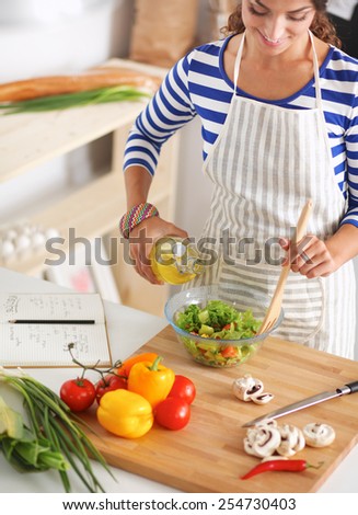 Smiling young woman  mixing fresh salad, standing near desk