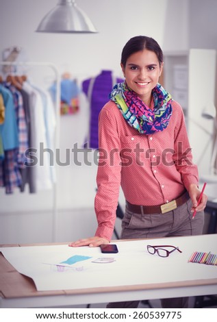 Young attractive female fashion designer working at office desk, drawing while talking on mobile