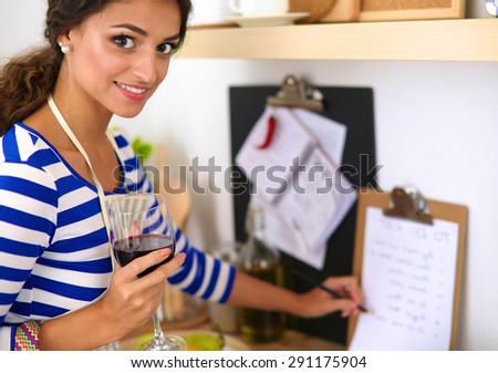 Young woman cutting vegetables in kitchen, holding a glass of wine