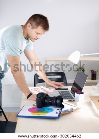 Male photographer standing near  the desk with laptop