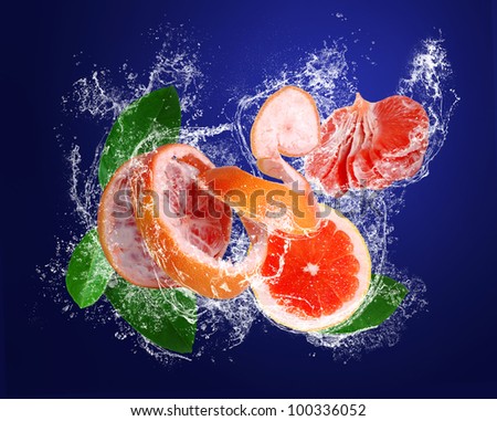 Grapefruit with peeled skin, leaves and segments in water drops on the dark blue background