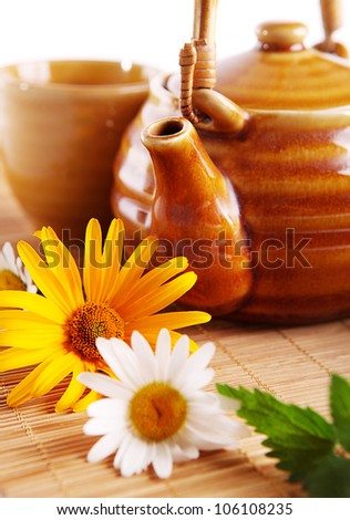 Closeup image of teapot and daisy flowers on the bamboo mat