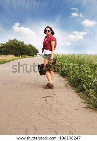 Girl auto-stop traveler with old suitcase on the road