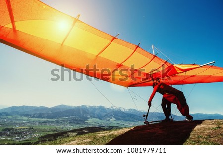 Man with hang-glider starting to fly from the hill top