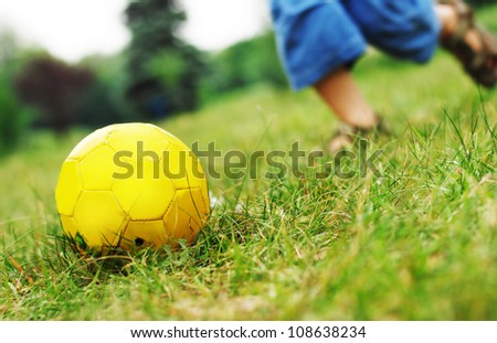 Image with local focus on yellow ball and running boy  legs