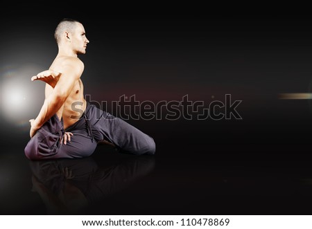Yong man doing yoga exercise on black mirrored background