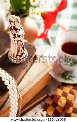 Still life with chess mini sculpture, old books, checkerboard cookies and cup of tea