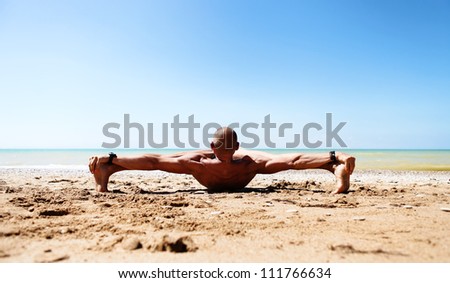 Muscular man doing stretching yoga pose at the sand beach